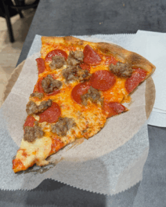 Pepperoni and sausage pizza slice with melted cheese on a paper plate in New York City
