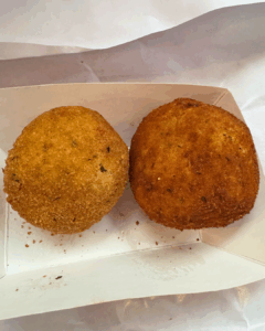 Two golden fried arancini served on a paper-lined tray