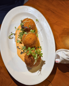 Crispy arancini served on a white plate with sauce and fresh herbs