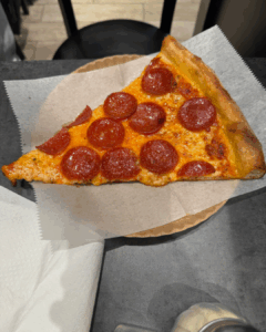 Pepperoni pizza slice with melted cheese on a paper plate in New York City