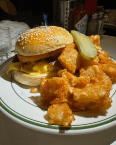 Breakfast sandwich with eggs and bacon served with crispy tater tots and a pickle