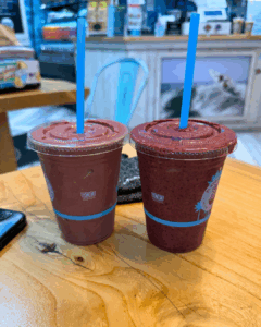 Two fruit smoothies in clear cups on a wooden table at Playa Bowls