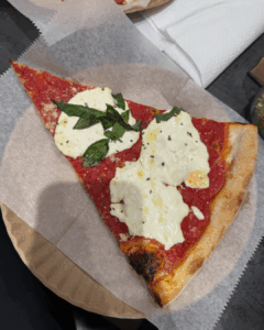 Margherita pizza slice with fresh mozzarella, tomato sauce, and basil on a paper plate