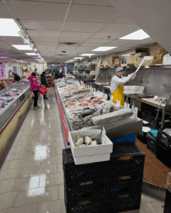 Seafood counter with whole fish on ice and a fishmonger preparing seafood at a New York City market