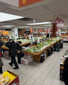 Produce section of an Asian grocery store with fresh vegetables and shoppers in New York City
