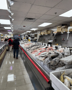 Wide view of a seafood market with fish displayed on ice inside an Asian grocery store in New York City