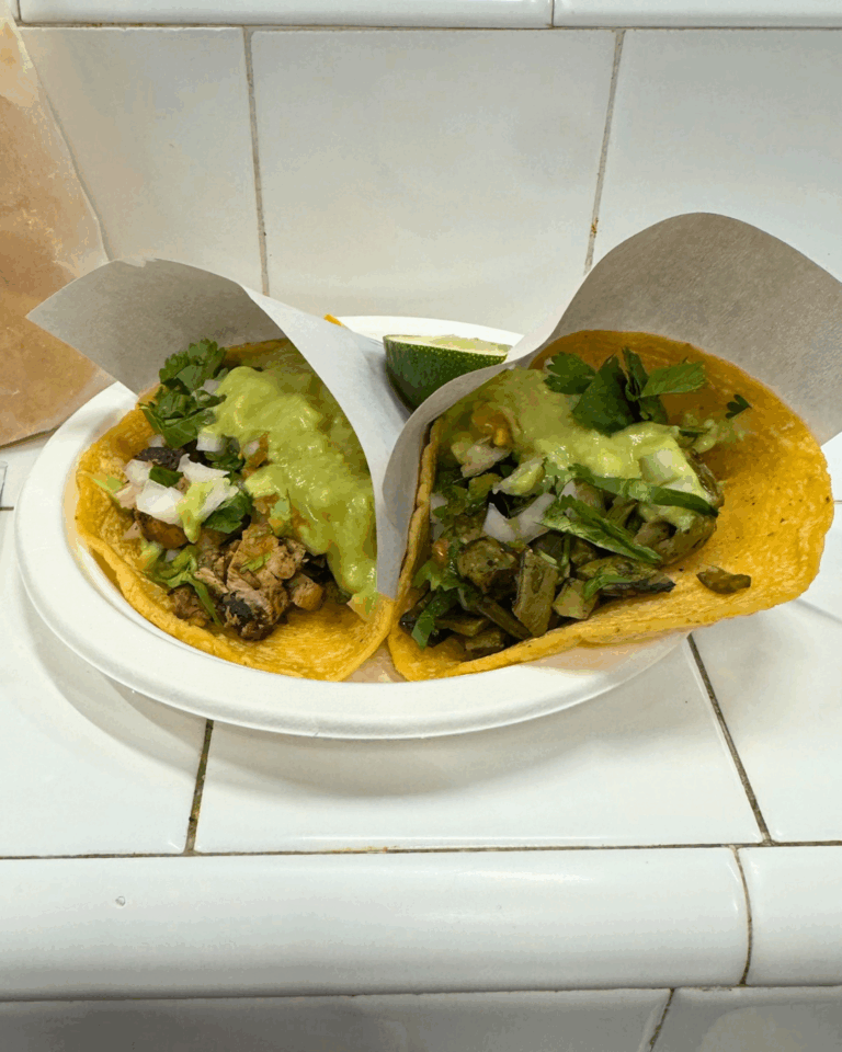 Two steak tacos with cilantro, onions, and avocado sauce on corn tortillas from a New York City taco shop