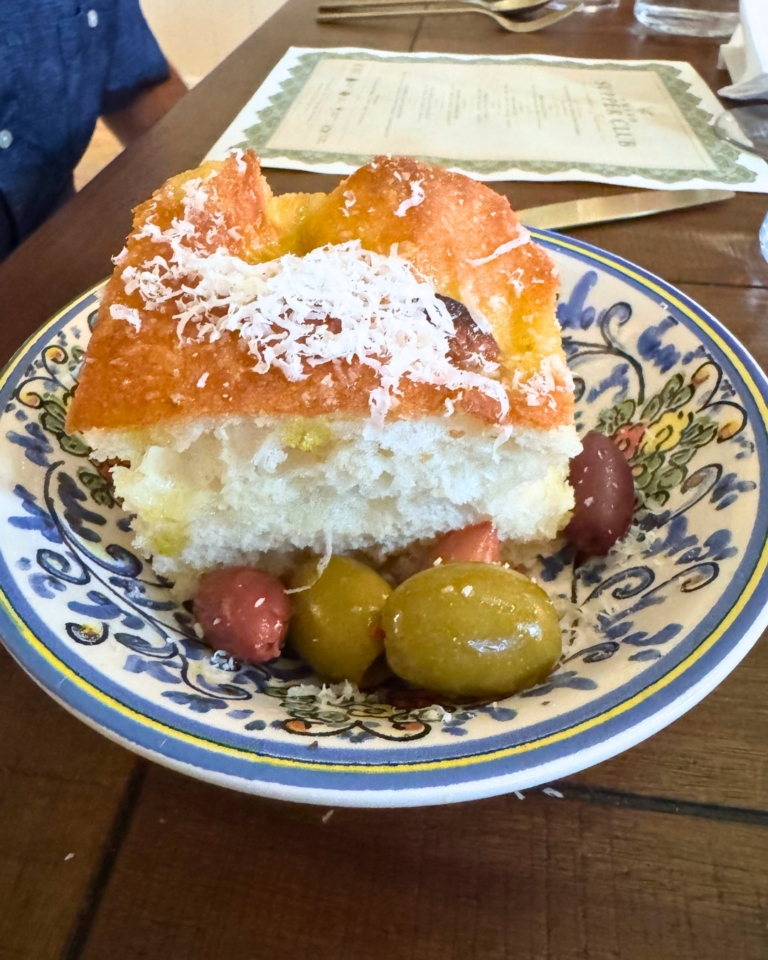 Warm homemade focaccia topped with grated Parmesan, served with seasoned Italian olives at Amaro Supper Club.